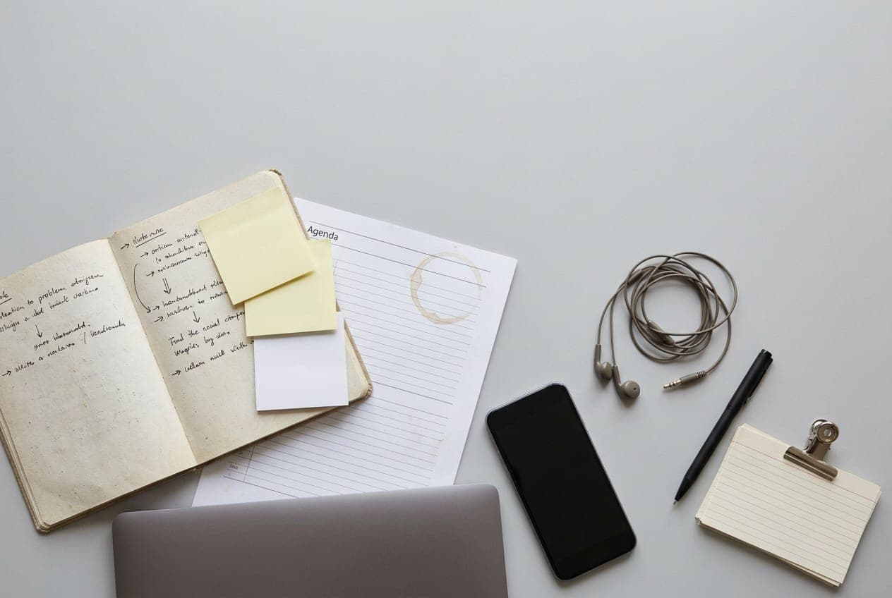 A desk at the end of a busy week: notebook, sticky notes, a printed agenda and a phone, scattered