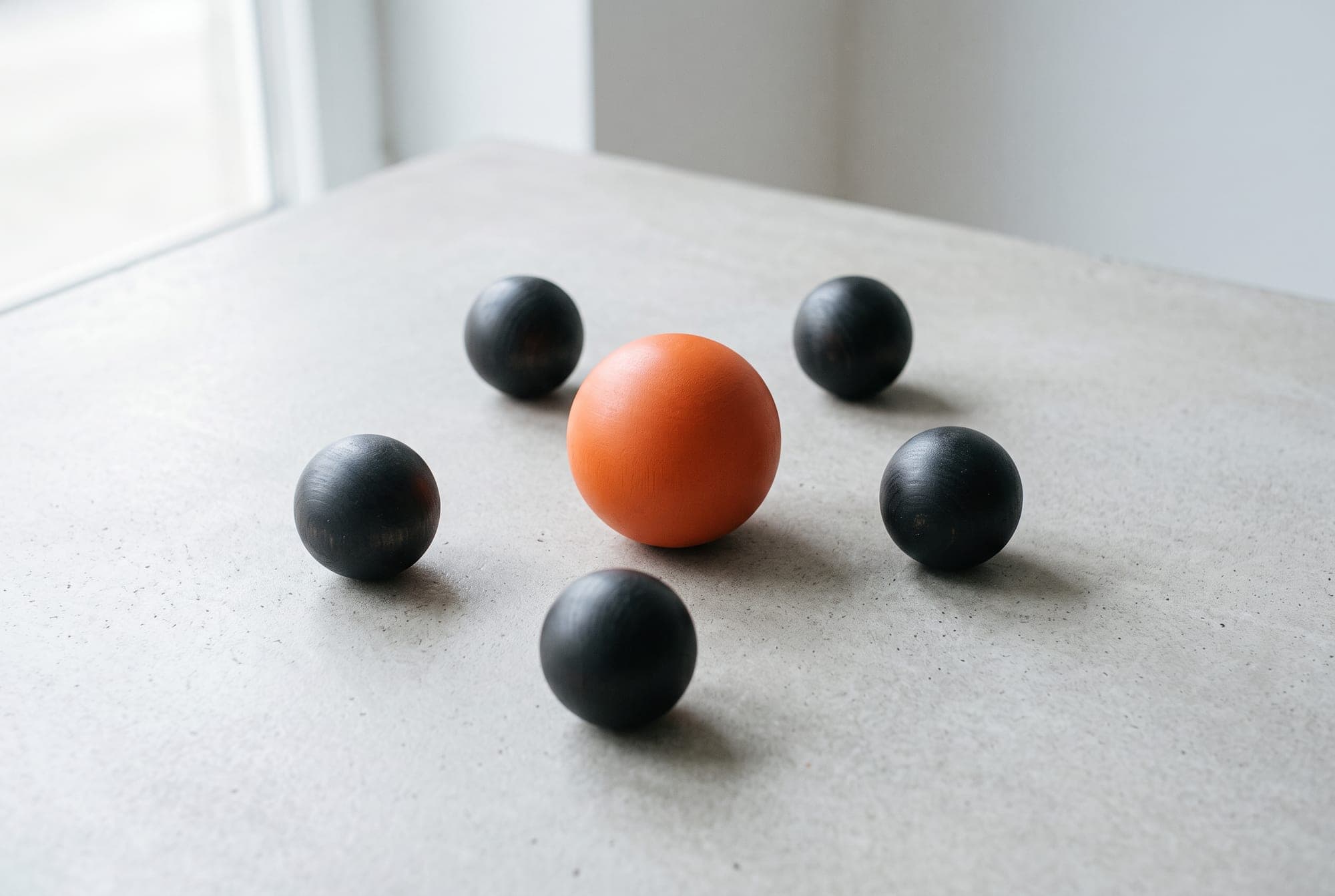 One orange sphere with five charcoal spheres around it on a grey table, laid out like the New Brain mark.