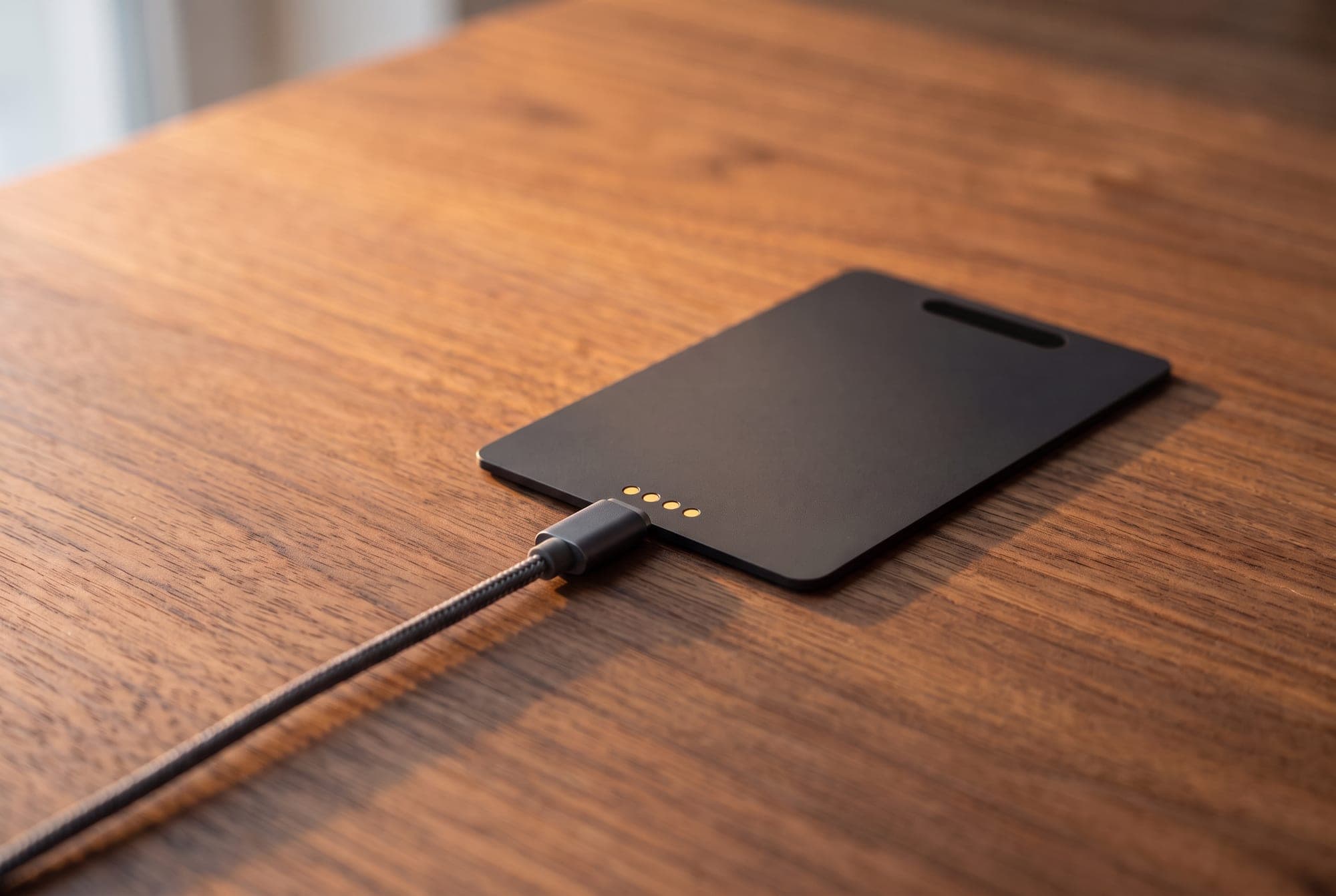 The back of New Brain Card on a desk with the magnetic charging cable clipped to its contacts